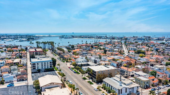 Aerial panoramic view of a coastal neighborhood with various buildings and a distant view of the sea.