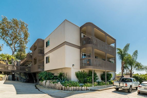 Front view of a multi-story building with covered balconies and surrounding greenery.
