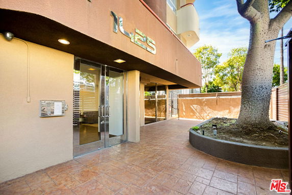 Front view of a building entry with glass doors and a tree nearby.