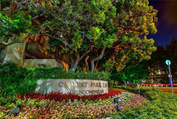 Front view of a building with a sign reading 'Century Park East Condominiums' surrounded by trees and flowers.