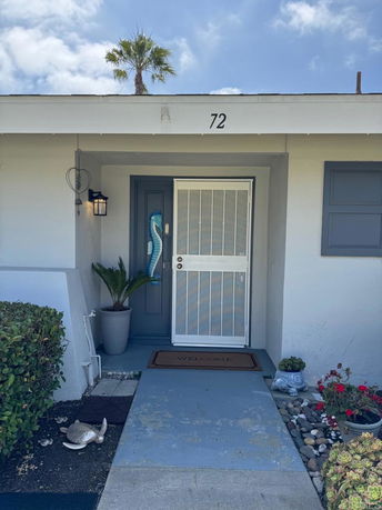 Front view of a single-story house entrance with a welcome mat and decorative plants.