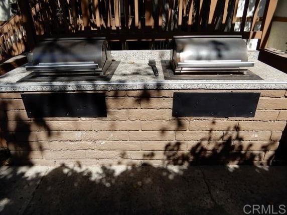 Outdoor view of a built-in barbecue grill with two metal grills and a countertop on a brick base.