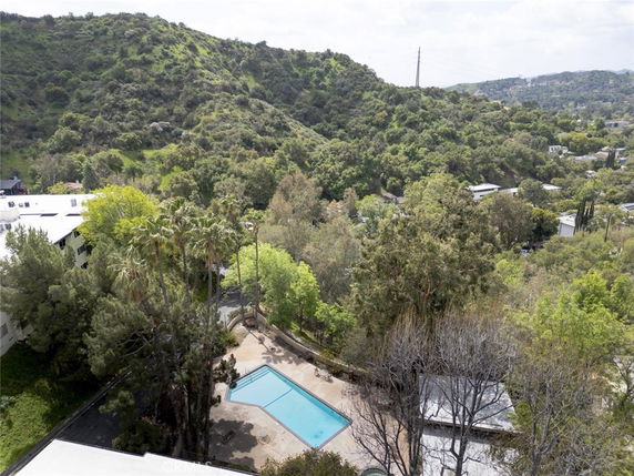Panoramic view of lush green hills with scattered buildings and a swimming pool visible below.