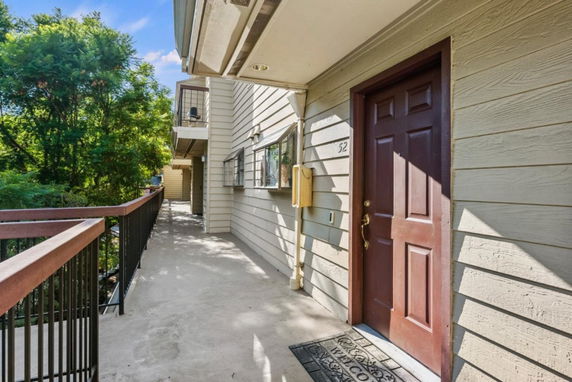Exterior view of an apartment building corridor with a wooden door and windows.
