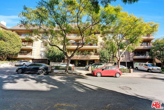 Front view of a multi-story residential building with balconies and trees.