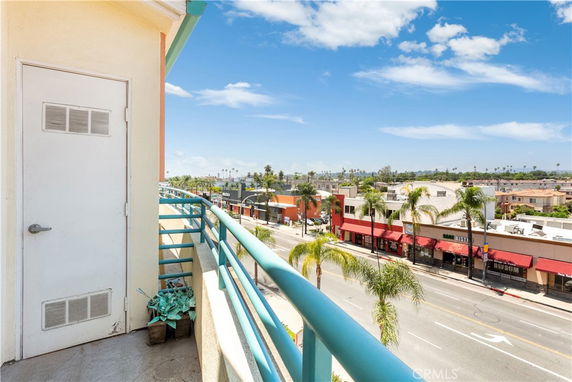 Panoramic view from a building balcony overlooking a street with palm trees and shops.