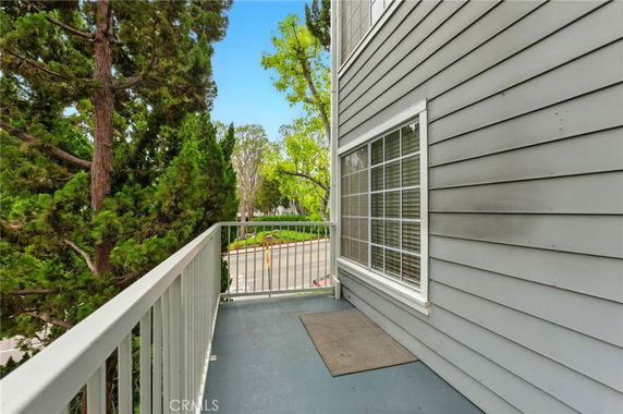 Side view of a building with a balcony overlooking a street and trees.