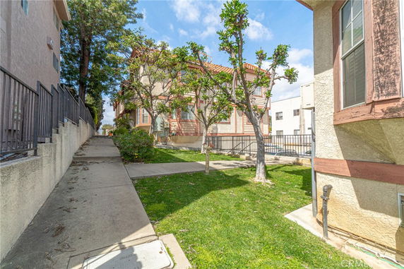 Side view of a multi-story residential building with a paved pathway and grassy area with trees.