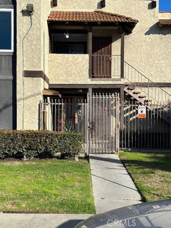 Front view of a multi-story building with a gated entrance and external staircase.