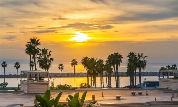 Panoramic view of a sunset over the ocean with palm trees and rooftops in the foreground.