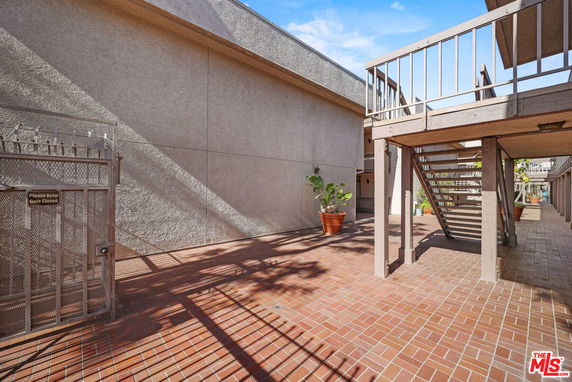 Outdoor area with brick flooring and stairway with metal railing.