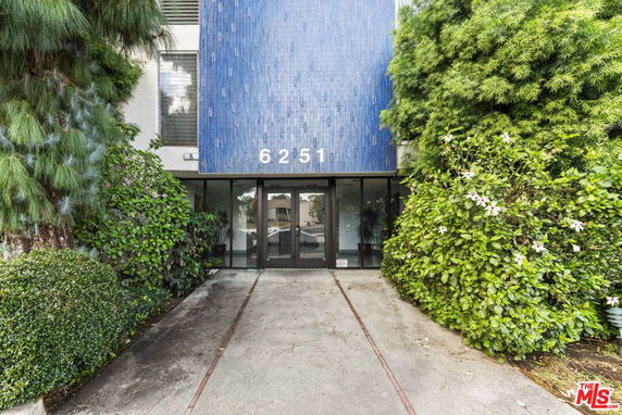 Front view of a building with a blue tiled facade and entrance surrounded by greenery.