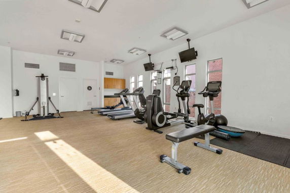 Interior view of a gym room with exercise equipment and windows.