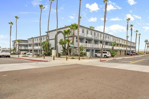 Front view of a multi-story building with balconies and tall palm trees.