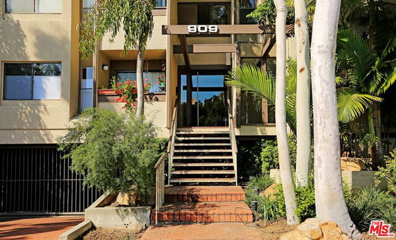Front view of a multi-story building entrance with stairs and plants.