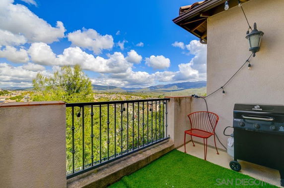 Balcony with grill and chair offering a panoramic view of hills and clouds.