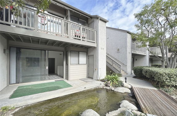 Front view of a two-story residential building with balconies and a small pond.