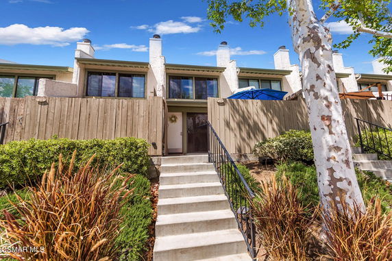 Front view of a two-story townhouse with a wooden fence and staircase leading to the entrance.