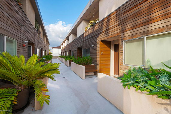 Exterior view of two-story residential buildings with wooden paneling and potted plants.