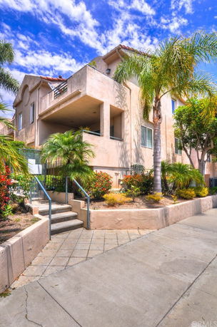 Front view of a multi-story house with a balcony and surrounding palm trees.