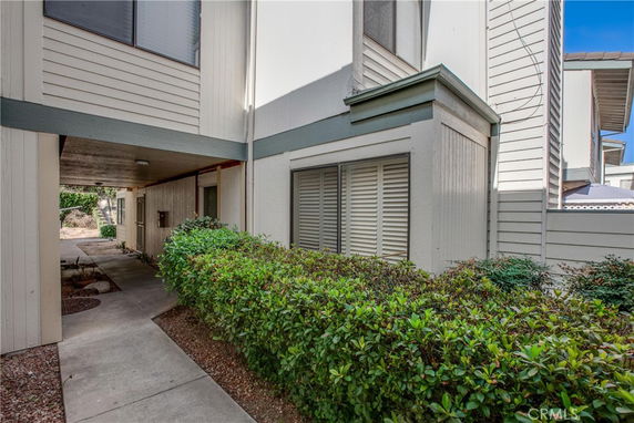 Partial view of a multi-story building exterior with a walkway and shrubs.
