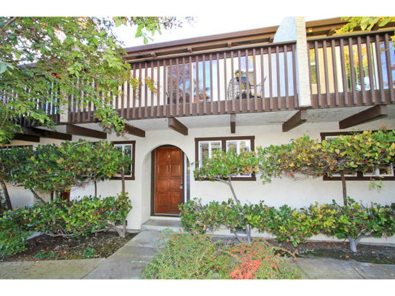 Front view of a two-story house with a wooden balcony and arched entrance.