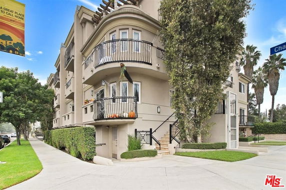 Front view of a three-story building with balconies and landscaped entry.