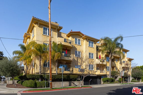 Front view of a multi-story residential building with balconies and palm trees.