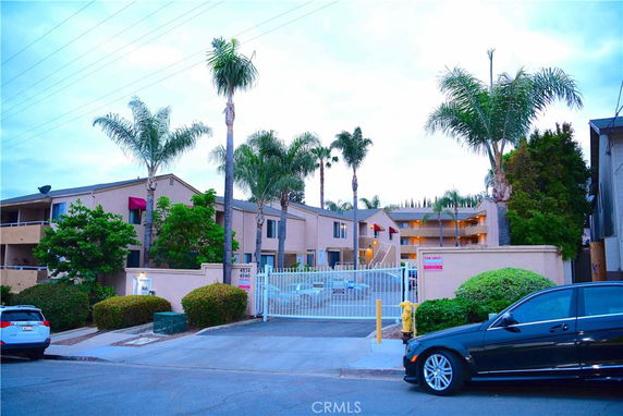 Front view of an apartment complex with palm trees and gated entrance.