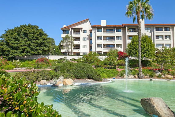 Front view of a multi-story residential building with a fountain and greenery in the foreground.