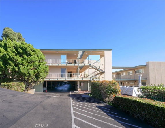 Front view of a multi-story apartment building with external staircases and open parking area.