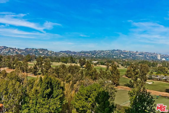 Wide panoramic view of a landscape with vegetation and distant hills under a blue sky.