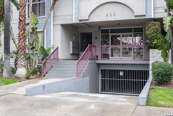 Front view of a residential building with stairs and an entrance to an underground parking area.