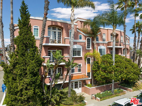 Front view of a four-story apartment building with a pink facade and numerous balconies.