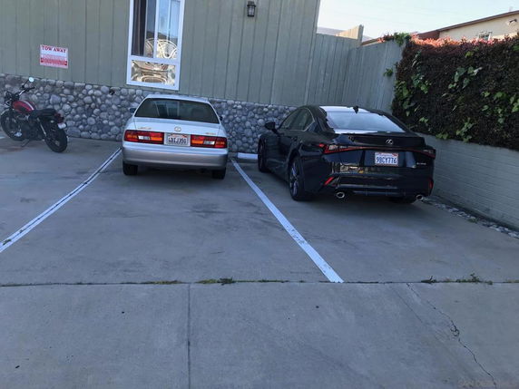 Outdoor parking area with two cars and a motorcycle parked.