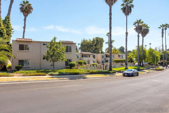 Front view of a two-story residential building with a tiled roof and windows, surrounded by palm trees and landscaping.