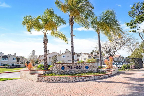 Front view of a town center building with palm trees and a stone sign in the foreground.