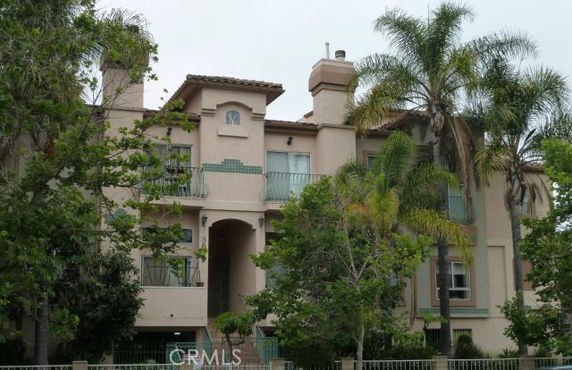 Front view of a multi-story residential building with balconies and surrounded by tall palm trees.