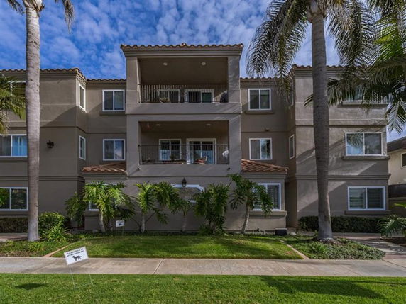Front view of a three-story residential building with balconies and palm trees.