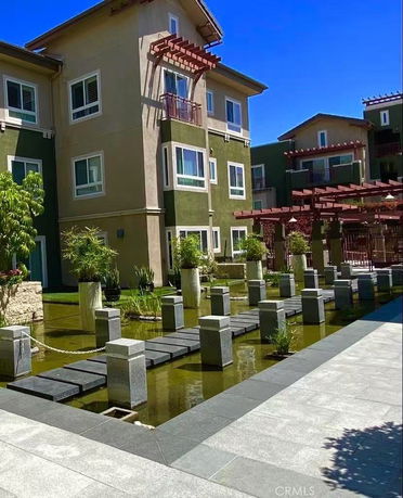 Front view of a multi-story residential building with decorative balconies and a water feature.