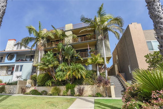 Front view of a multi-story building with balconies and palm trees in front.
