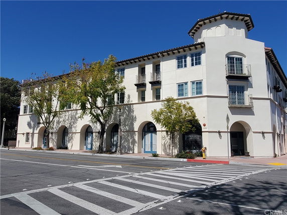 Front view of a three-story building with arched entryways and a corner tower.