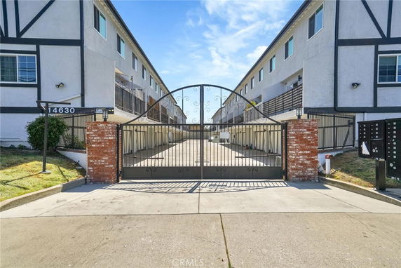 Front view of a gated multi-story building with a driveway.