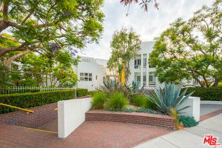 Front view of a multi-story building with white facade and surrounding greenery.