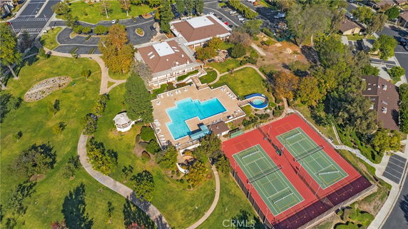 Aerial view of a large recreational area featuring a swimming pool, tennis courts, and surrounding greenery.