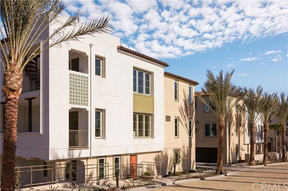 Front view of multi-story modern townhouses with balconies and palm trees.