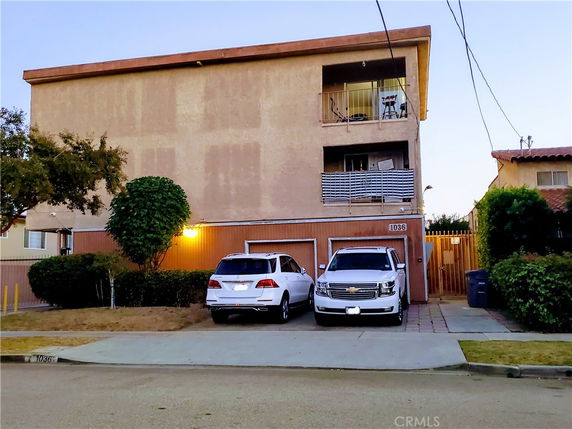 Front view of a multi-story building with balconies and two cars parked in front.
