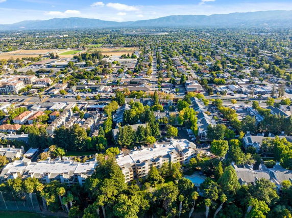 Aerial panoramic view of a residential neighborhood with surrounding greenery and distant mountains.