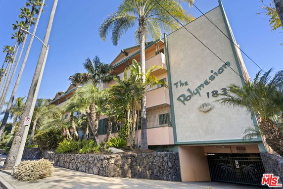 Front view of a multi-story residential building with tropical plants and a sign reading 'The Polynesian'.