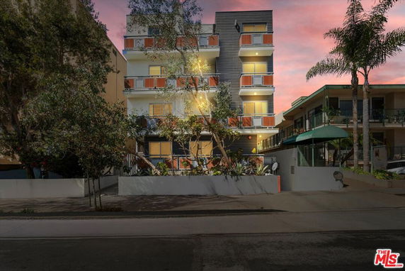 Front view of a multi-story building with balconies and trees at sunset.